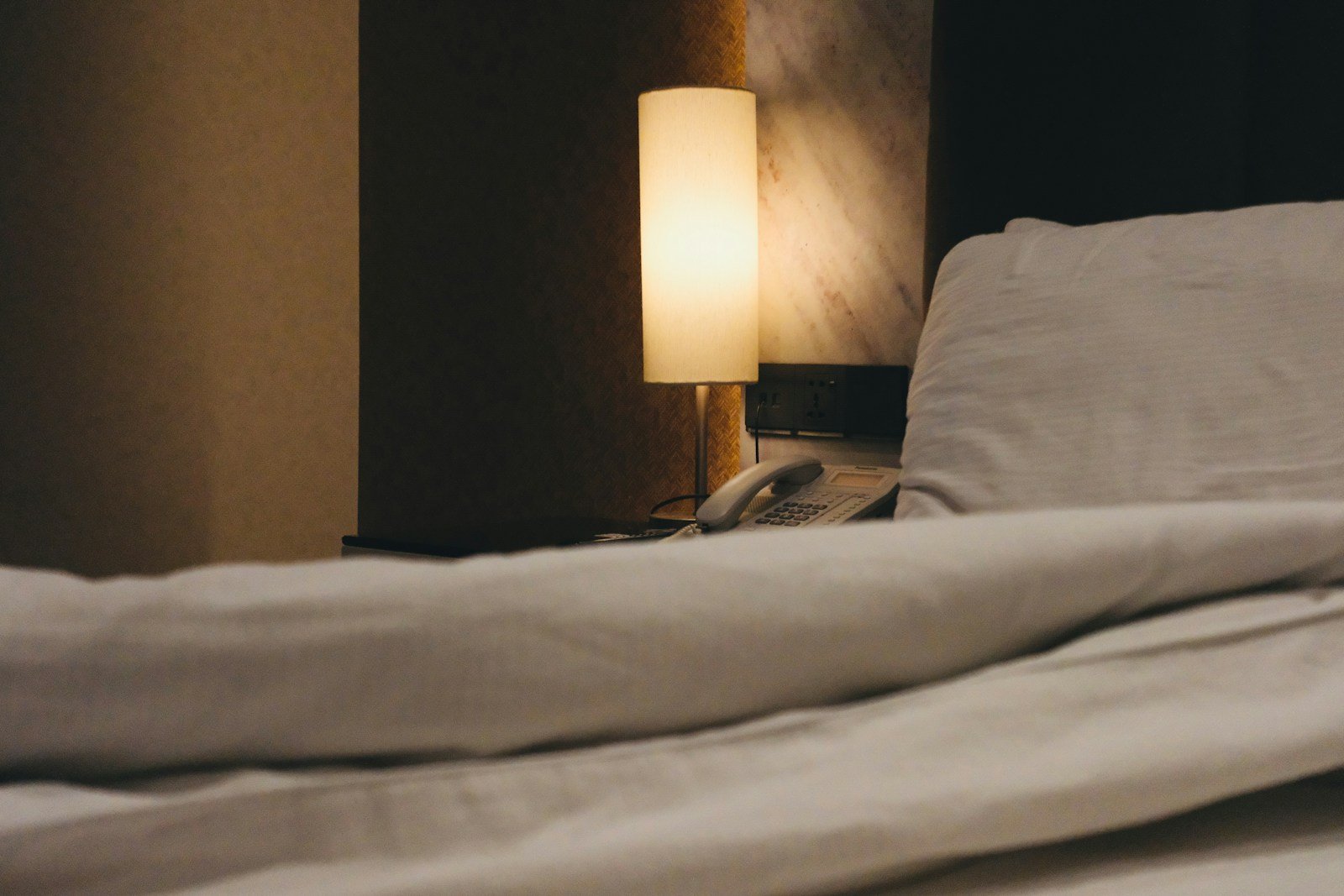 Bedside lamp glowing at night beside a telephone on the nightstand
