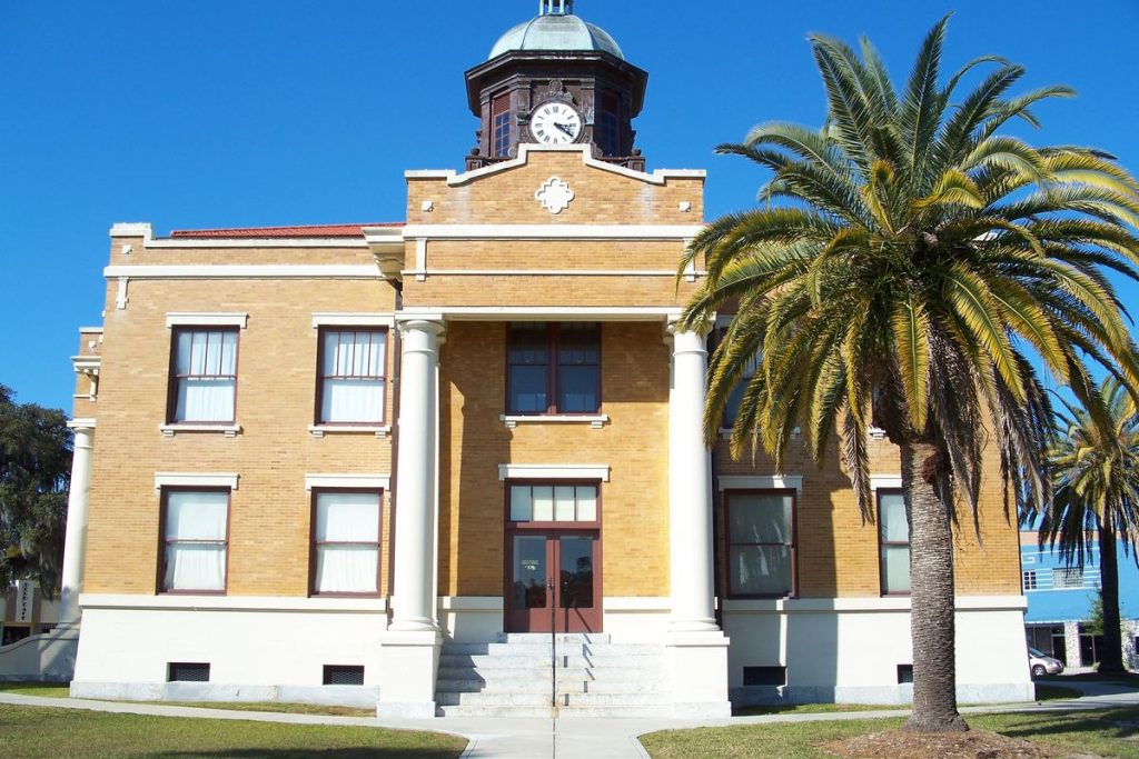 Historic yellow-brick Old Citrus County Courthouse in Inverness, with white columns, a clock tower, and a palm tree