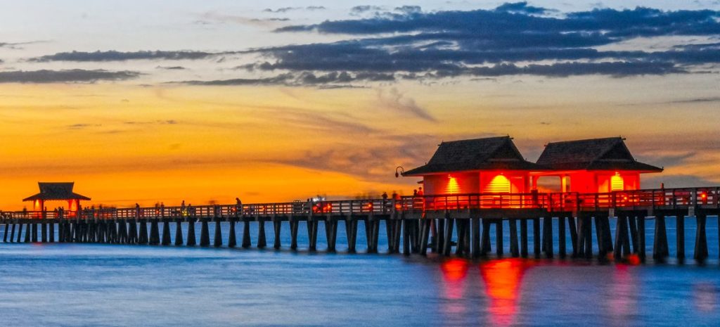 Naples Pier stretching into the Gulf at sunset, its pavilions lit against the evening sky