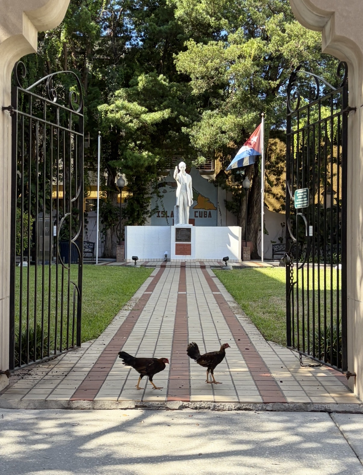 Gated entrance to a park in Ybor City, Tampa, with a statue and two roosters on the walkway